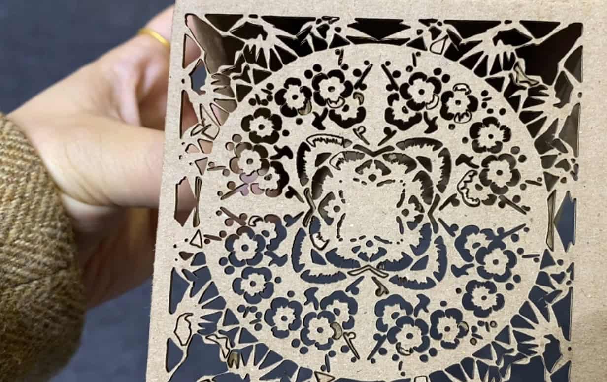 A display table showing various materials all processed by a CO2 laser: a cardboard box, an acrylic sign, an engraved piece of wood, and a cut piece of fabric