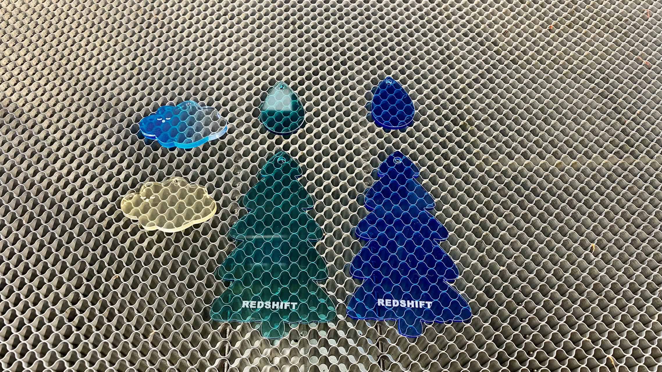 A festive collage of engraved gifts: a wooden spoon, an acrylic ornament, a leather wallet, and a black stainless steel tumbler.