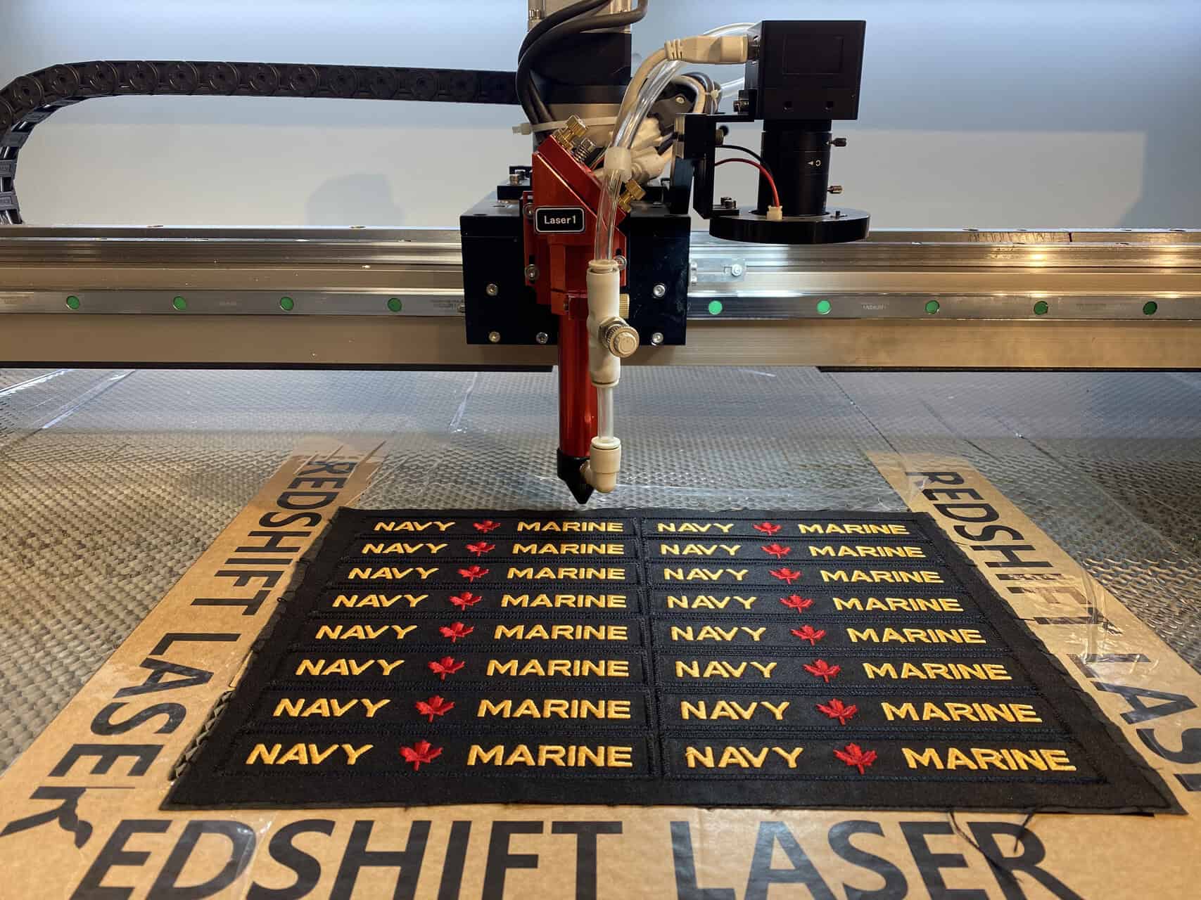 A clean, well-lit image of a Redshift Laser machine with a large cutting bed and a visible camera system on the head