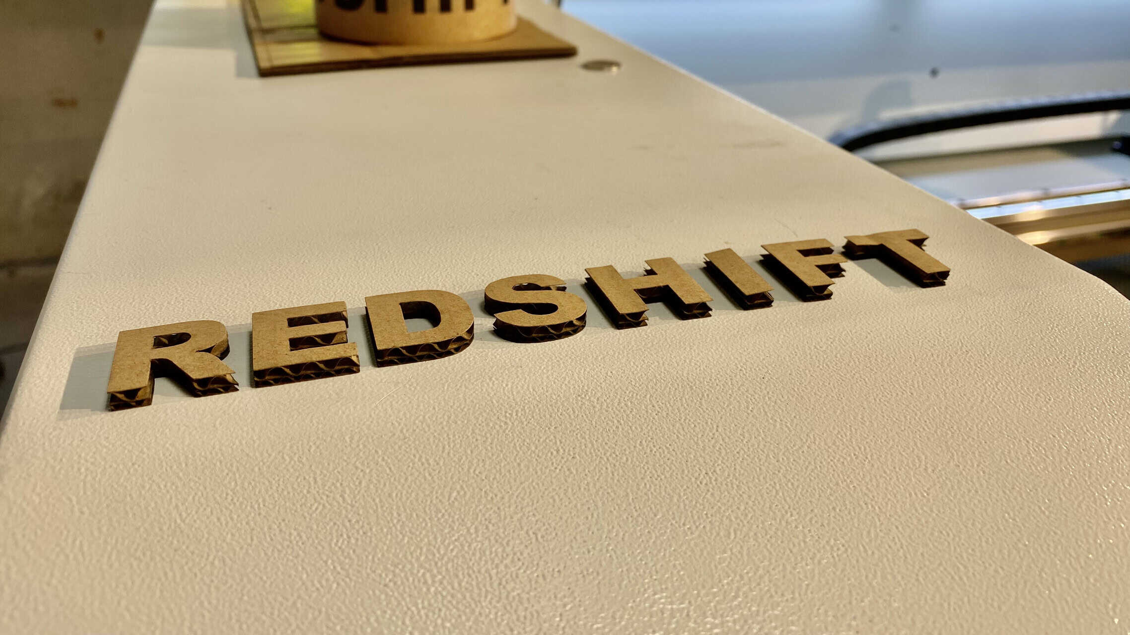 A compact CO2 laser cutting machine with its lid open, showing a sheet of cardstock on the cutting bed